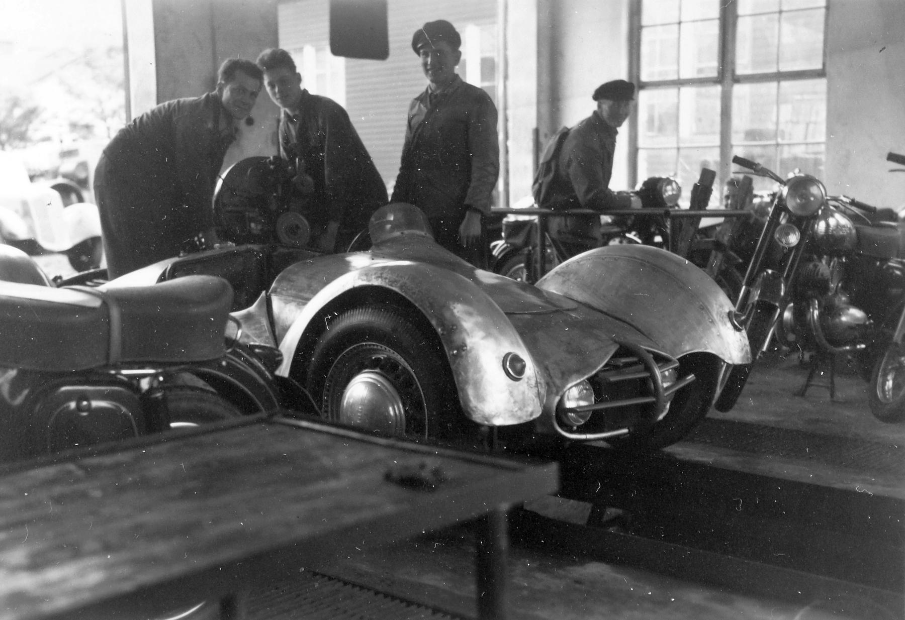 a black and white photo of a car being worked on the chassiss - File:Workshop, motorcycle, worker, a